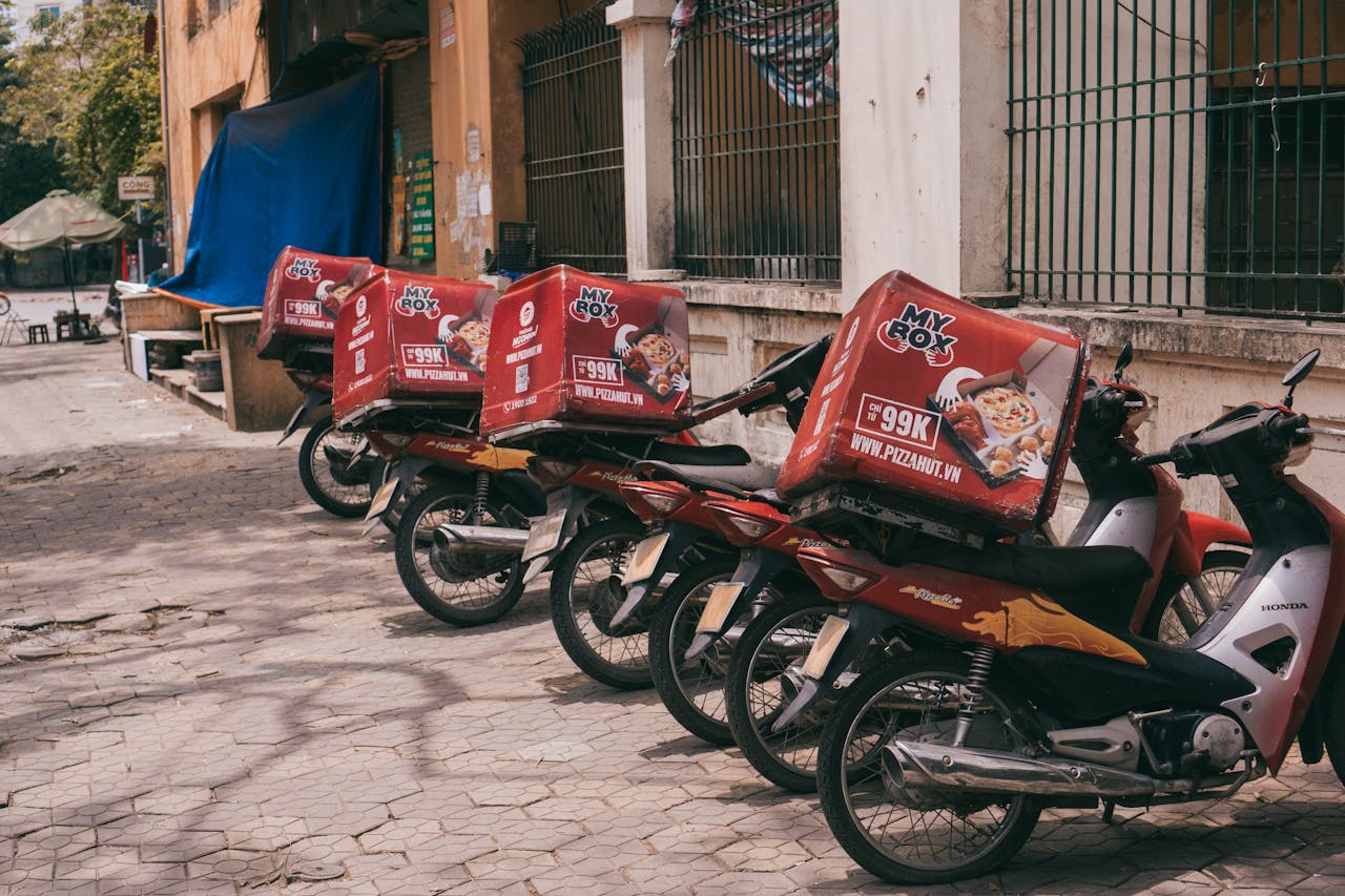 services-03 Motorbikes with branded delivery boxes parked on an urban sidewalk, showcasing food delivery services.